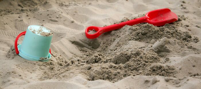 Children's sand play with a blue bucket and red shovel on a beach. Harmless appearance but potentially dangerous.