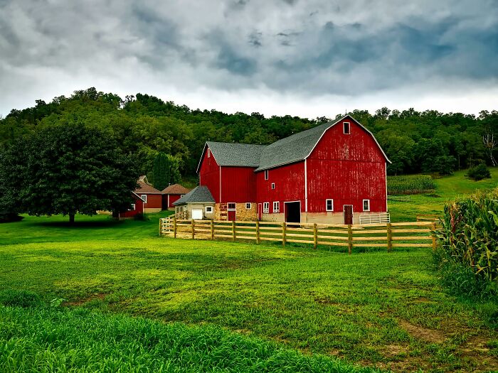 Red barn on lush green farmland under cloudy sky.