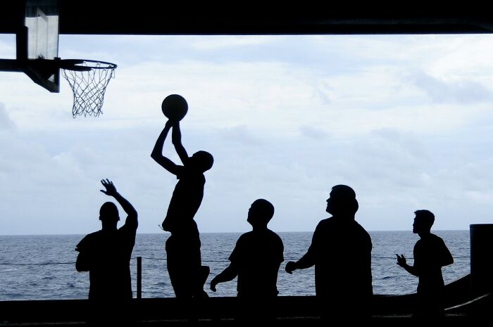 Silhouettes playing basketball near the ocean, capturing a mysterious and unusual scene with a sky backdrop.