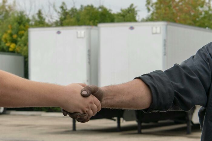 Two people shaking hands with trucks in the background, symbolizing adult realizations and agreements.