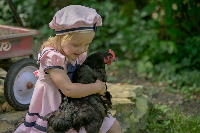 Child in pink dress cuddling a chicken outdoors, illustrating kids labeled as weird ones for unique behaviors.