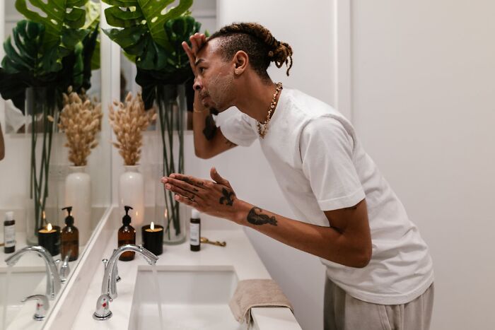 Man in white shirt grooming in front of mirror, emphasizing personal care, one of the non-s****l things that turn women on.