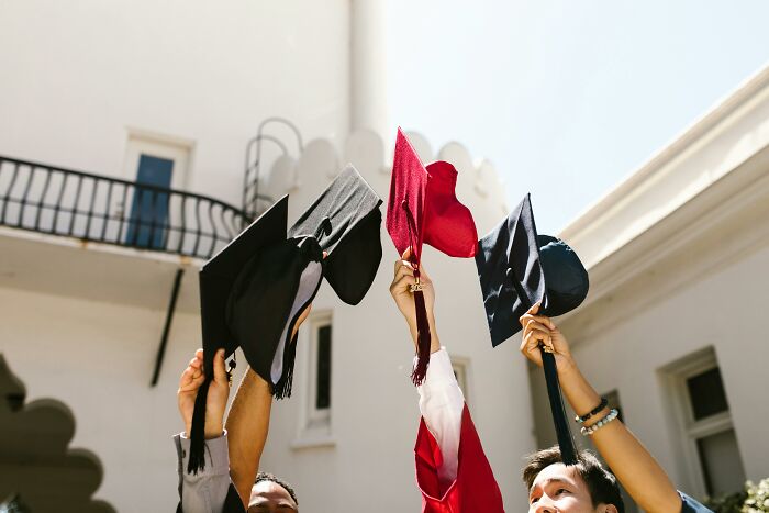 Graduates raising caps in celebration against a school building, symbolizing crazy school memories.