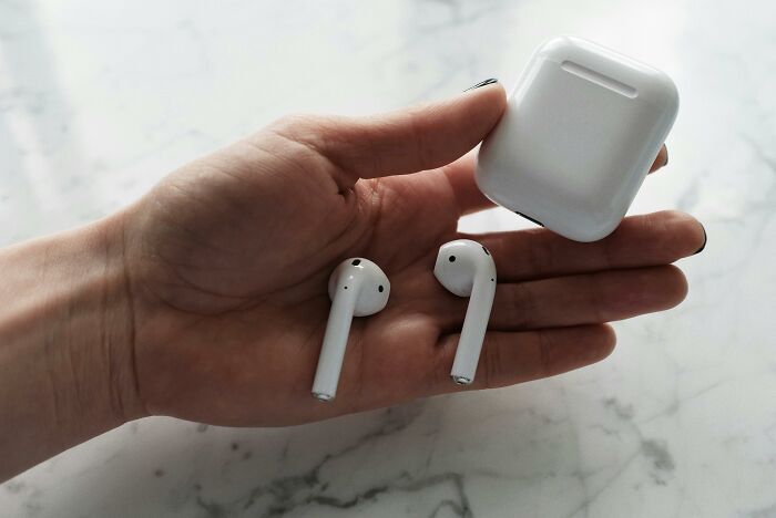 A hand holding wireless earbuds and a case on a marble surface, relevant to controversial-conspiracy-theories.