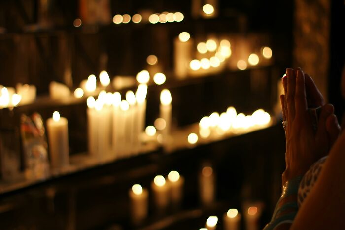 Candles in a dimly lit space representing adult realizations, with a person praying in the foreground.