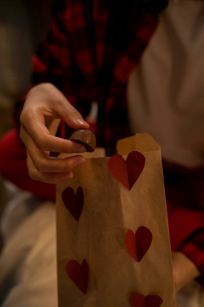 A person in a plaid shirt placing a chocolate in a gift bag with heart designs, illustrating non-s****l things that turn women on.
