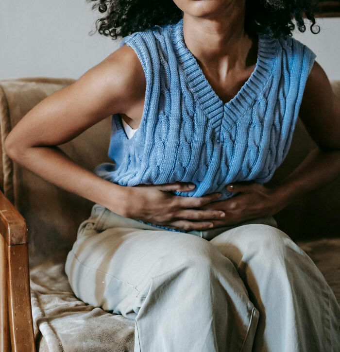 Person in a blue sweater sitting, holding their stomach, suggesting reasons for significant weight gain.