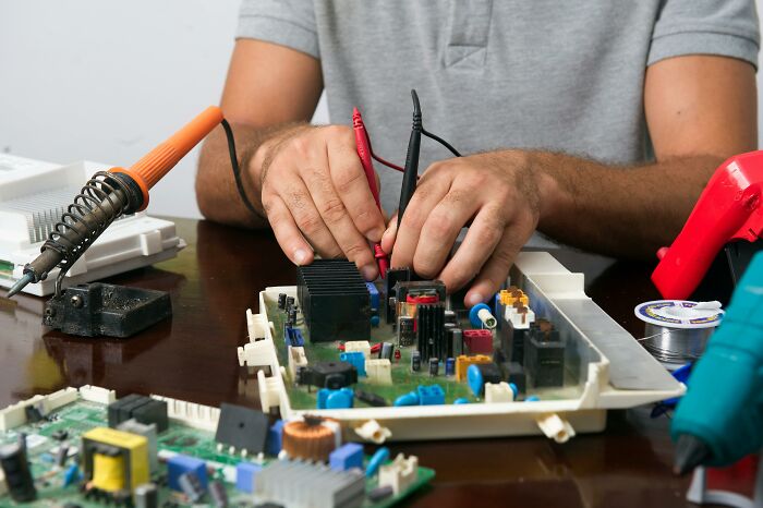 Person working with electronic components, avoiding trends to focus on hands-on electronics repair on a wooden table.