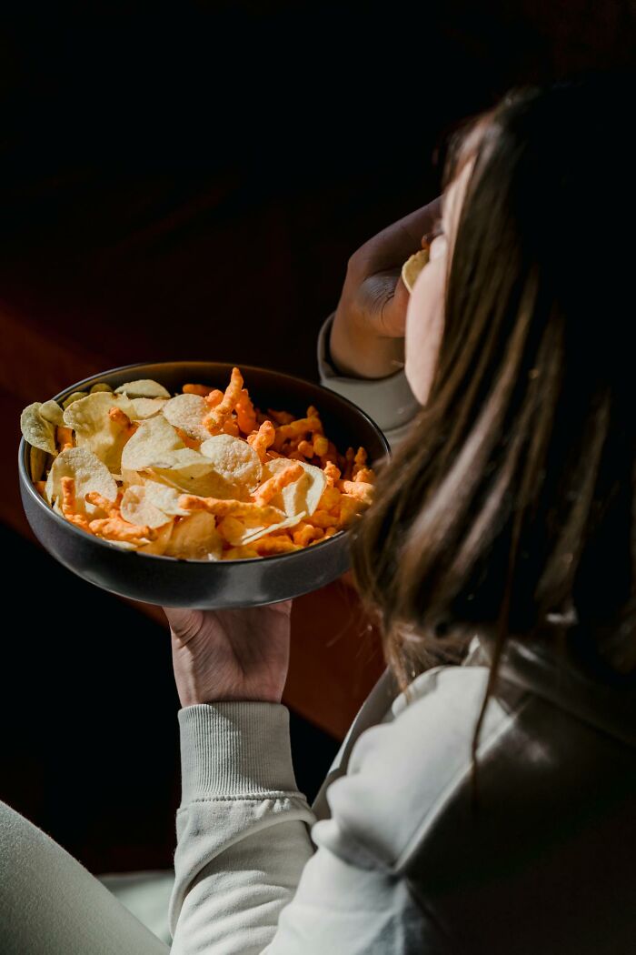 Person eating chips from a large bowl, highlighting weight gain factors related to snacking.