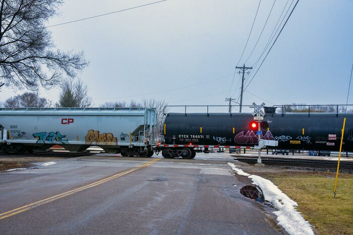 Freight train crossing a rural road on a cloudy day with graffiti, capturing a scene of unexplainable and creepy stillness.