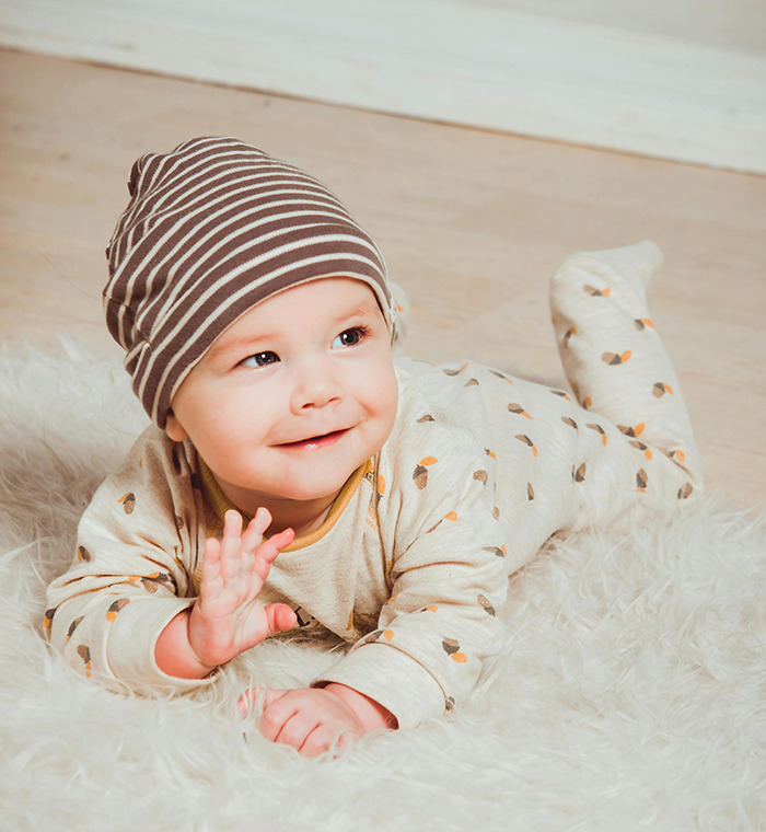 Baby from Generation Beta smiling on a soft rug, wearing a striped hat and patterned outfit.