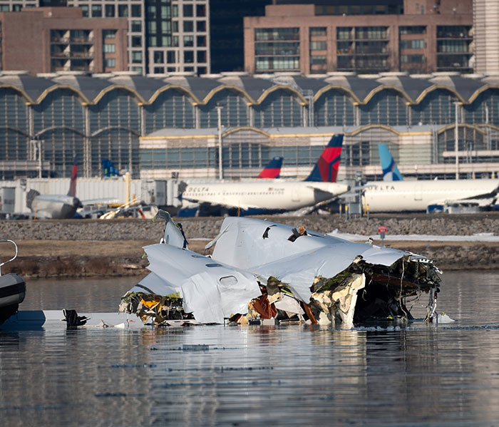 Plane crash debris on water with airport and planes in the background.