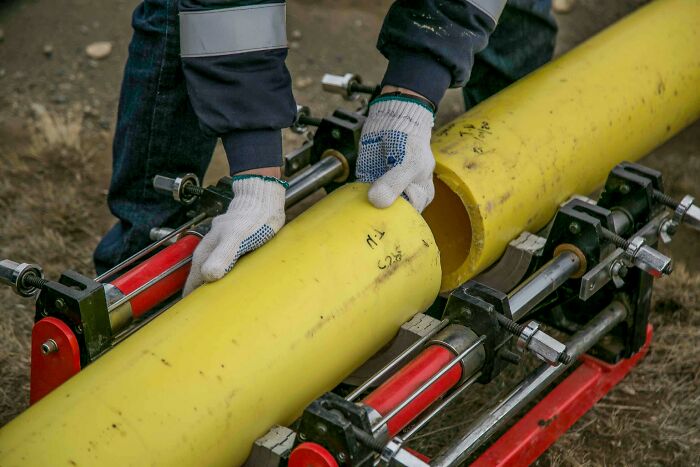 Plumbers handling large yellow pipe with safety gloves in a yard operation.