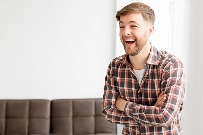 Man laughing in a plaid shirt in a living room, related to fake lottery ticket prank. Man laughing in a plaid shirt in a living room, related to fake lottery ticket prank.