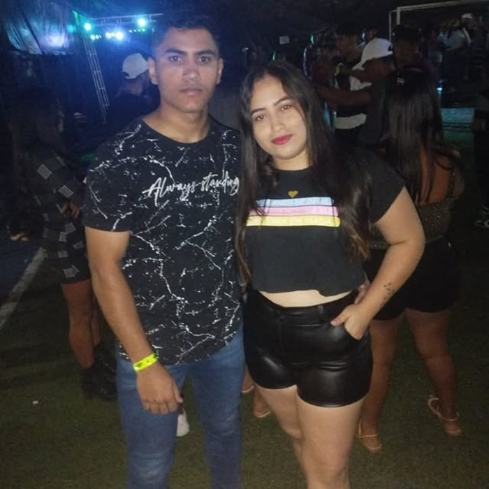 Joyce Sousa Ara&uacute;jo and her partner posing together at a nighttime event, with people in the background.