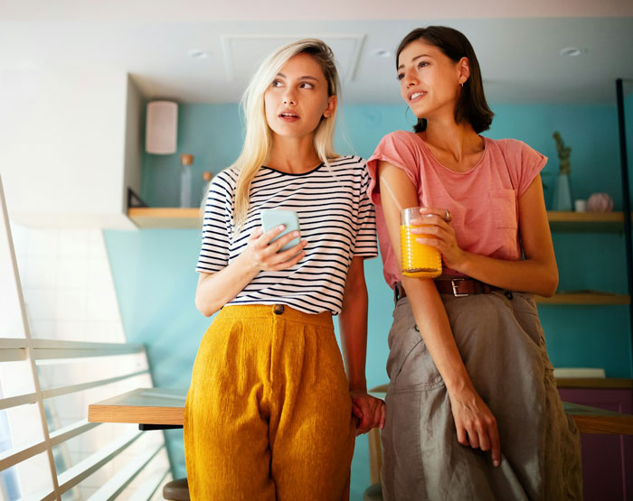 Two women casually chatting in a vibrant café, holding drinks and wearing stylish outfits. Two women casually chatting in a vibrant café, holding drinks and wearing stylish outfits.