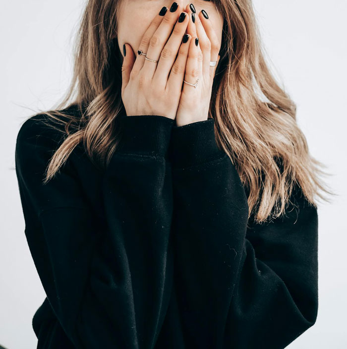 Woman covering her face with hands, wearing a black sweater, conveying a sense of embarrassment or shock. Woman covering her face with hands, wearing a black sweater, conveying a sense of embarrassment or shock.