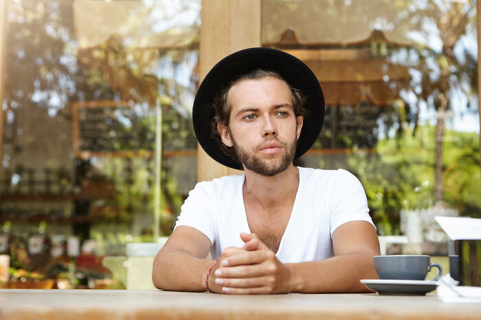 A man in a white shirt and hat sitting thoughtfully at a cafe, illustrating psychological tricks' impact.