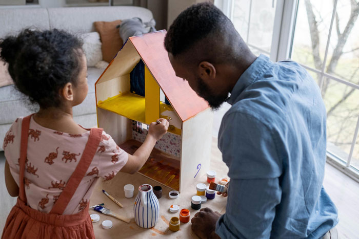 Man and child painting a replica house model together with various paints on a table. Man and child painting a replica house model together with various paints on a table.