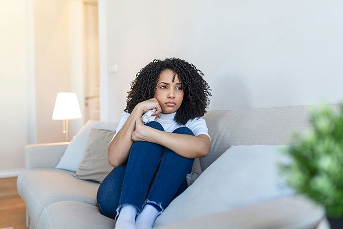 Woman sitting thoughtfully on a couch, reflecting on a friend's wedding uninvitation dilemma.
