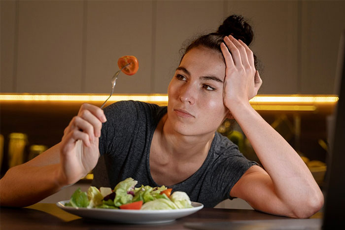Teen frustrated over dinner, holding a fork with tomato, green salad in front. Allergy issue with sister-in-law's meals. Teen frustrated over dinner, holding a fork with tomato, green salad in front. Allergy issue with sister-in-law's meals.