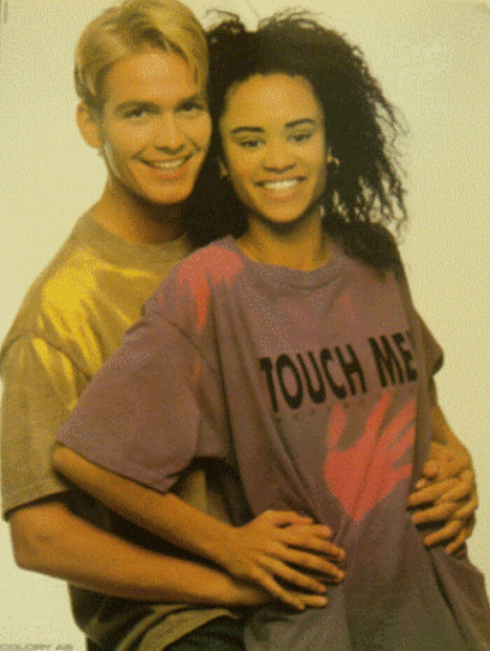Two people in vibrant 80s fashion, one in a gold shirt and the other in a colorful "Touch Me" T-shirt.