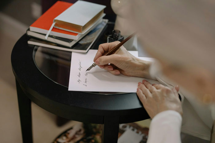 Person writing a letter on a table with books, related to a cat and puzzle incident with a roommate.