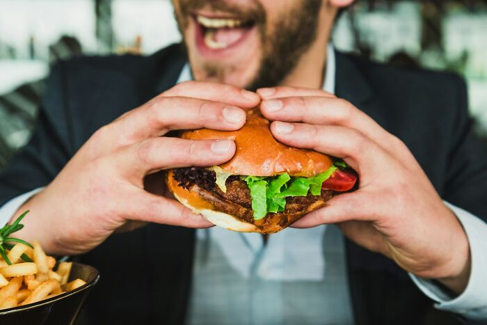 Man holding a burger, smiling broadly, with fries on the side, illustrating weight gain reasons.