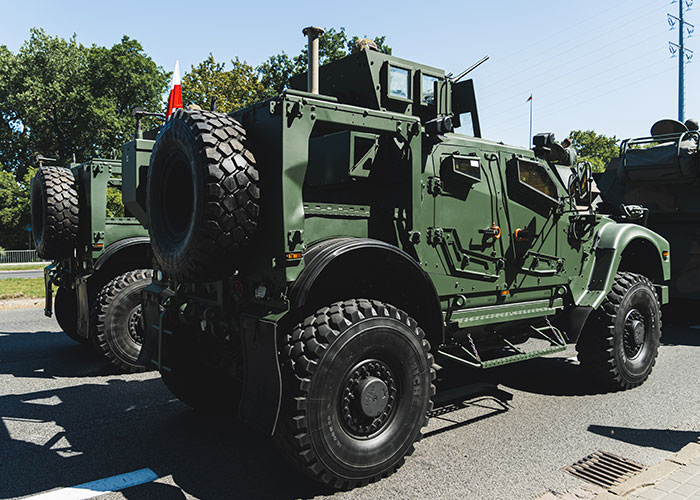 Military armored vehicles on a street in one of the scariest cities, with green trees in the background.