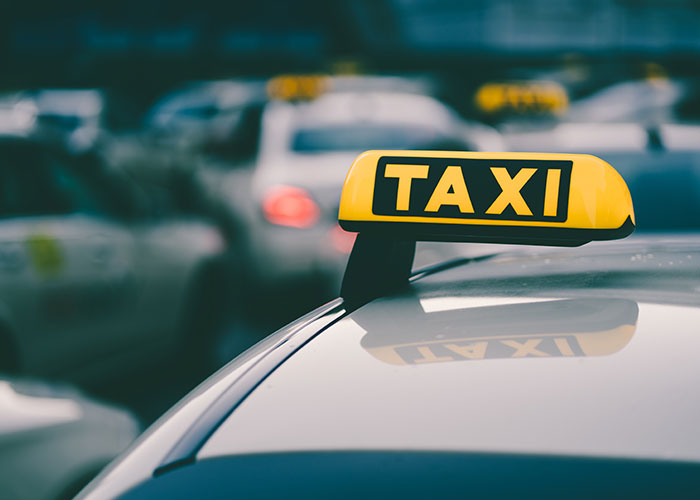 Yellow taxi sign on top of a car in urban setting, reflecting city atmosphere.