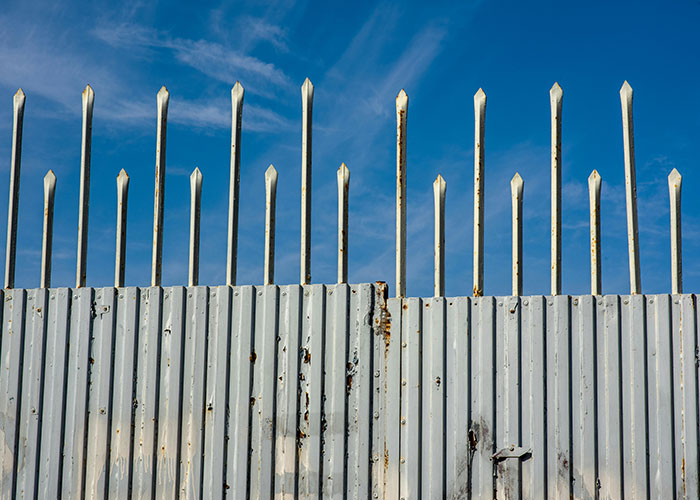 Tall spiked fence against a clear sky, representing urban danger in the scariest cities.
