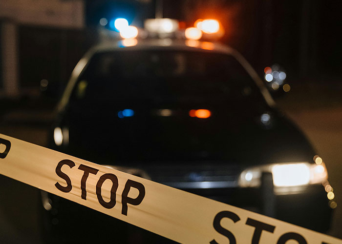 Police car with flashing lights behind "STOP" tape in a dark, eerie city street, evoking images of the scariest cities.