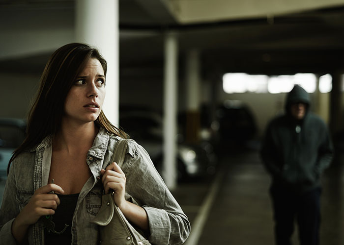 A woman in a parking garage looks worried with a hooded figure approaching, depicting fear in scariest cities.