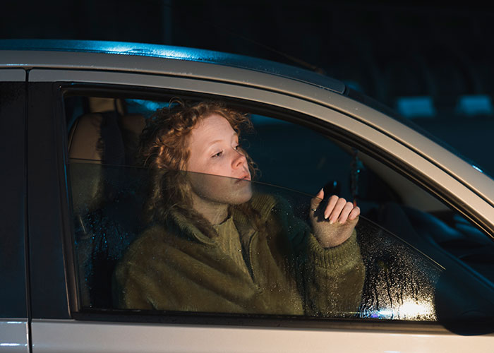 Person in a car looking out the window at night in a potentially scary city environment.