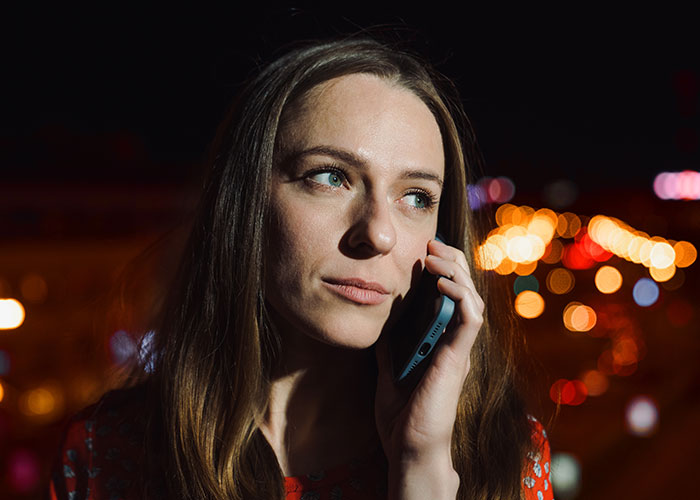 Woman with long hair on a phone, city lights in the background, illustrating a scene in one of the scariest cities.