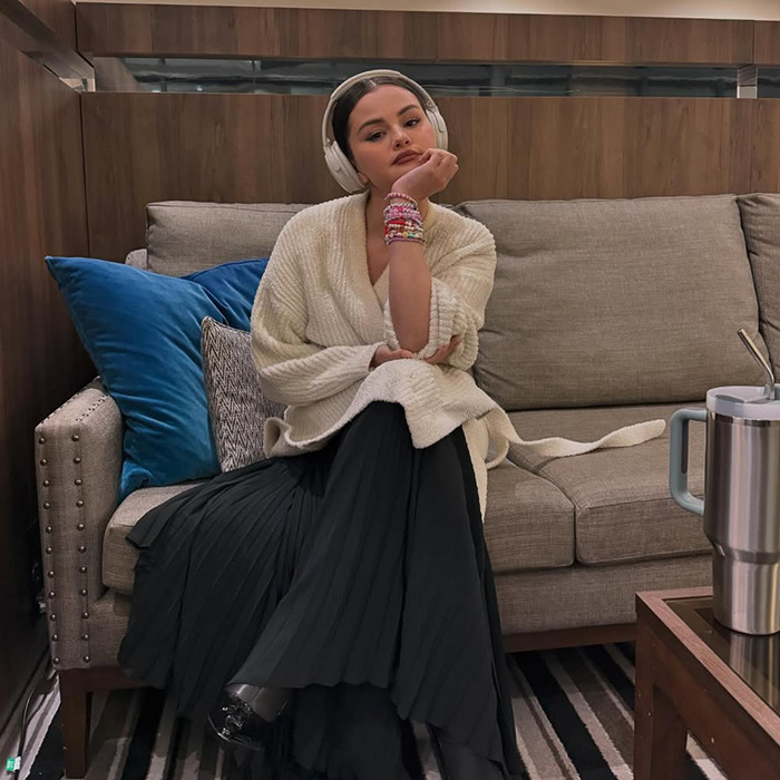 Selena Gomez sitting on a couch, wearing headphones and a cozy outfit, exuding a calm demeanor.