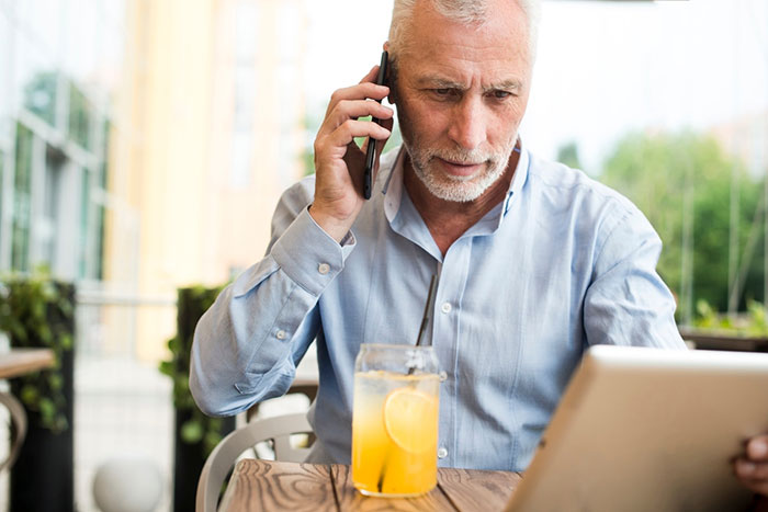 Elderly man on a phone call, using a tablet at a cafe with a lemon drink. Elderly man on a phone call, using a tablet at a cafe with a lemon drink.