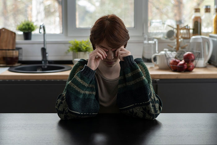 Woman sitting at a kitchen table, wearing a green sweater, looking down, related to spoiled brat controversy. Woman sitting at a kitchen table, wearing a green sweater, looking down, related to spoiled brat controversy.