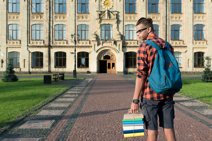 Young man with a backpack holding books, standing in front of a historical building on a sunny day. Young man with a backpack holding books, standing in front of a historical building on a sunny day.