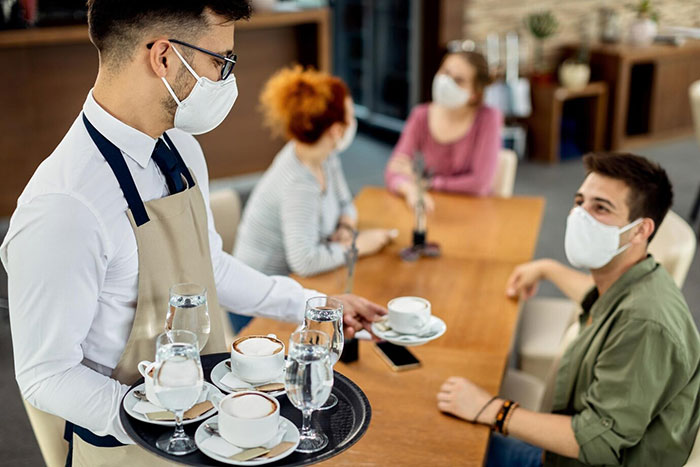 Waiter serving drinks to three people at a cafe, all wearing face masks. Waiter serving drinks to three people at a cafe, all wearing face masks.