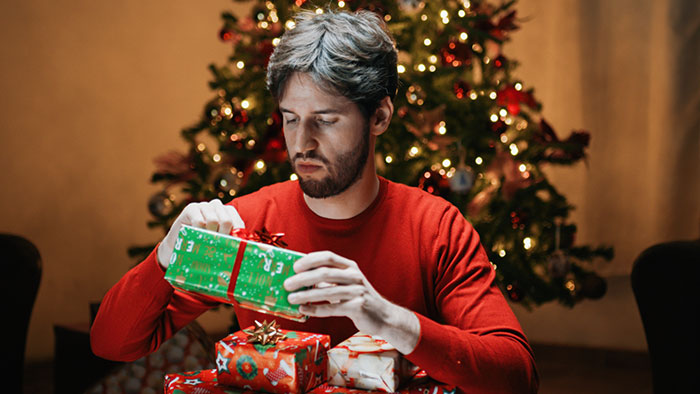 Man in red shirt wrapping gifts near Christmas tree. Man in red shirt wrapping gifts near Christmas tree.