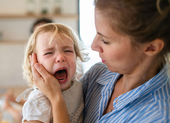 Mother comforting crying child, expressing frustration.