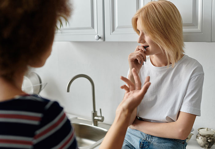 Two women in a kitchen have a discussion about a baby, one gesturing and the other looking thoughtful. Two women in a kitchen have a discussion about a baby, one gesturing and the other looking thoughtful.