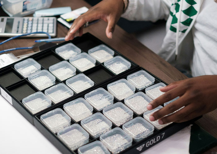 Person sorting small containers, possibly with beads, on a table with a calculator nearby. Person sorting small containers, possibly with beads, on a table with a calculator nearby.