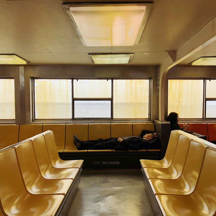 Person sleeping on a ferry bench, capturing the sleepmaxxing trend in a quiet public space.