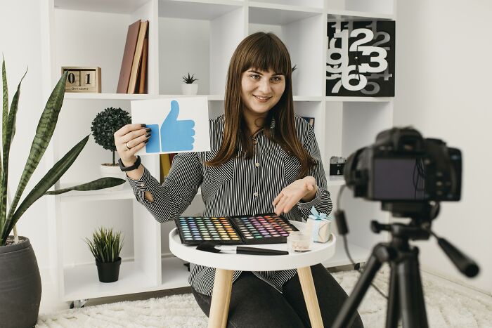 A woman presenting remotely with a camera, showcasing a thumbs-up sign, symbolizing high-paying remote jobs.