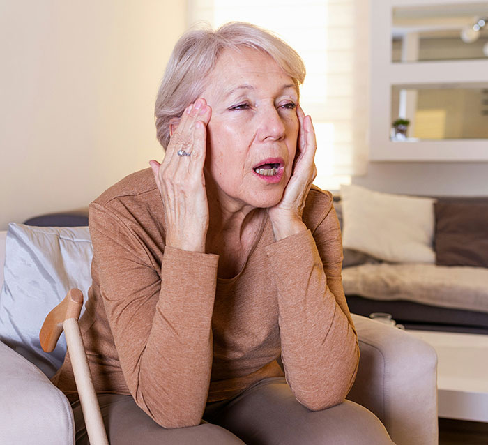 Elderly woman sitting on a sofa, appearing surprised, with a cane beside her. Elderly woman sitting on a sofa, appearing surprised, with a cane beside her.