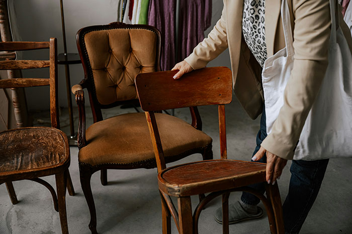 Woman arranging heirlooms, holding a wooden chair in a room with vintage furniture. Woman arranging heirlooms, holding a wooden chair in a room with vintage furniture.