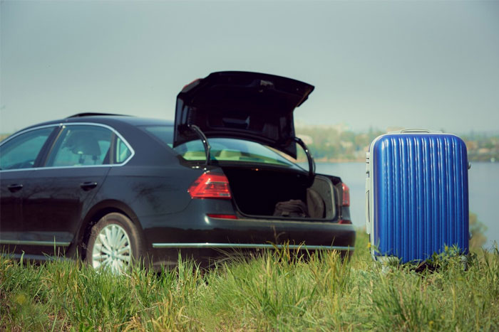 Black car with open trunk parked near water and blue suitcase standing on grass, timestamped pictures concept.