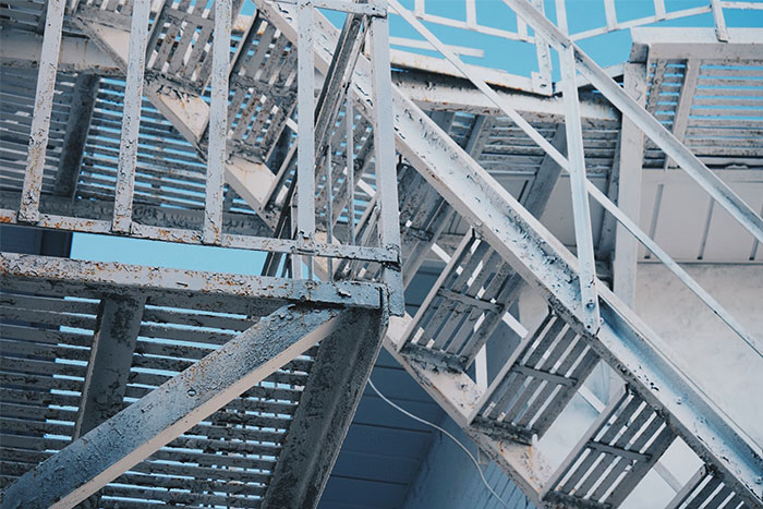 Rusty metal fire escape stairs with intersecting lines and a clear blue sky in the background. Timestamped pictures concept.